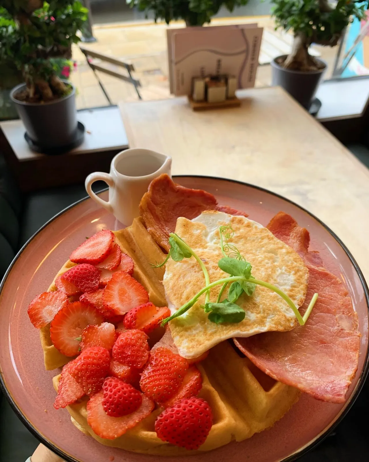 Waffle topped with fresh strawberries alongside fried egg and bacon.