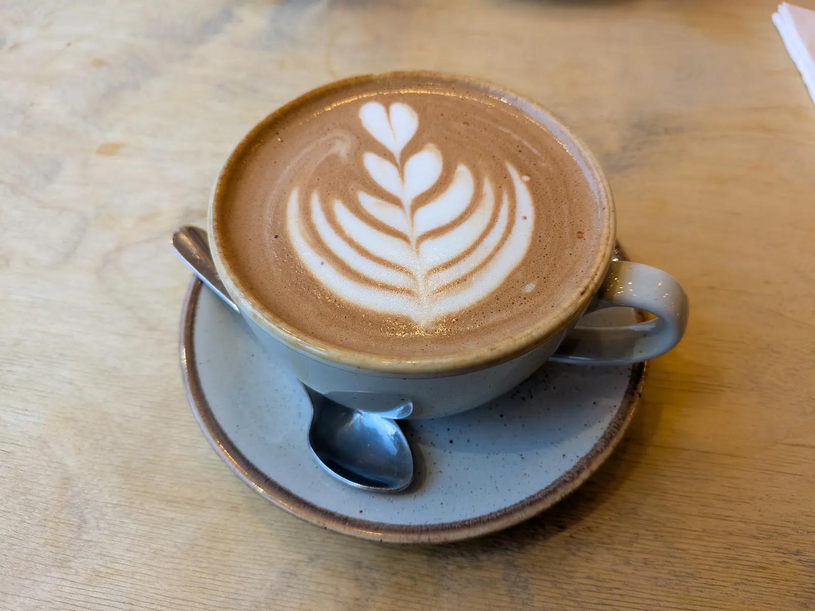 Flat white with leaf latte art in a stoneware cup.